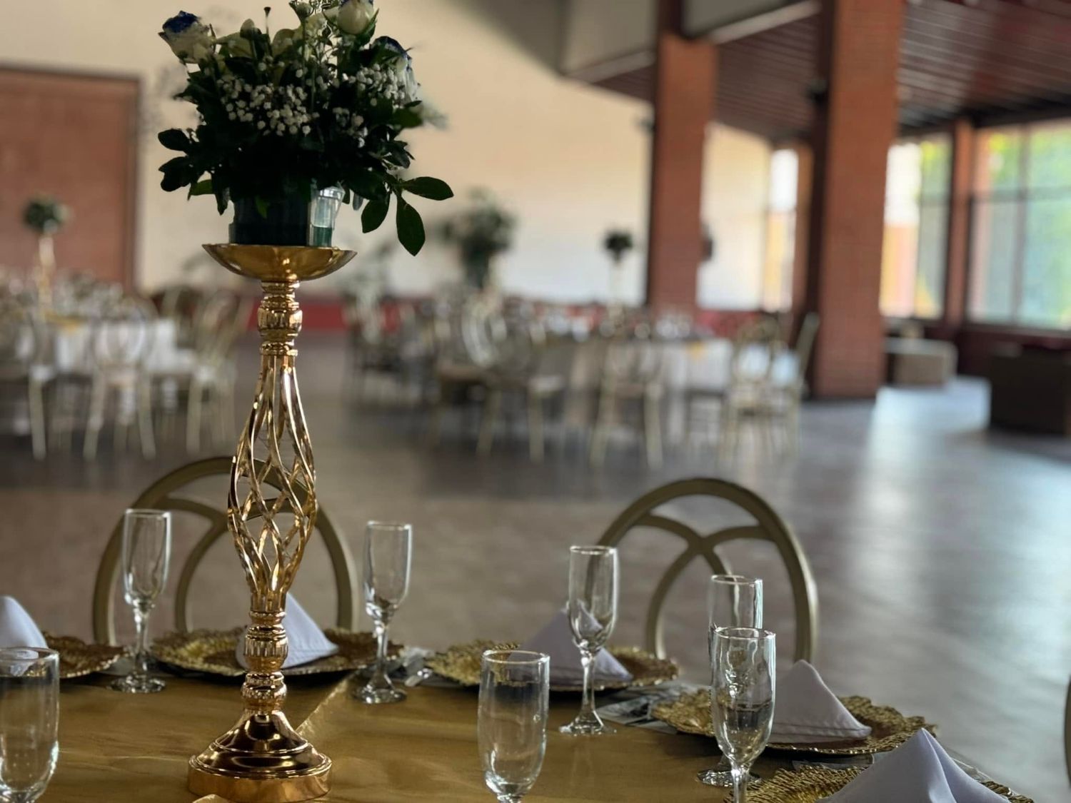 Centro de mesa dorado con rosas y follaje natural en salón de eventos
